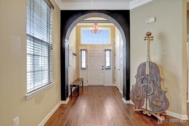 entrance foyer with a chandelier, arched walkways, hardwood / wood-style flooring, baseboards, and ornamental molding