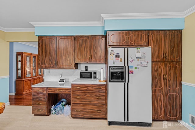 kitchen featuring white refrigerator with ice dispenser, crown molding, stainless steel microwave, light countertops, and light wood finished floors