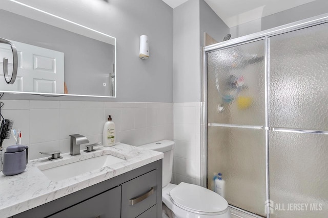 bathroom with a shower with door, vanity, tile walls, and toilet