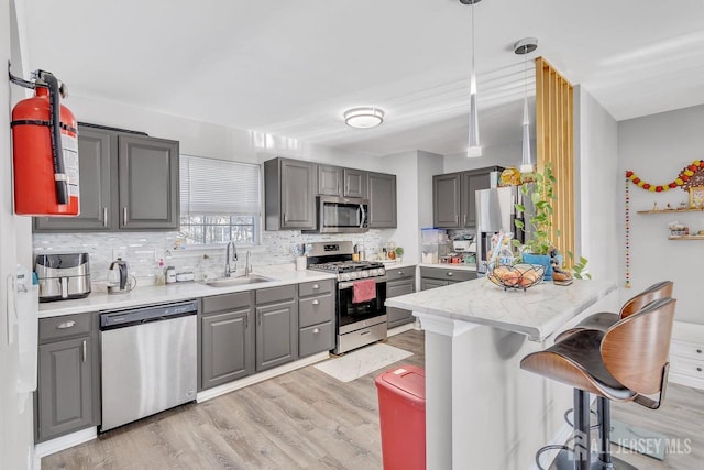 kitchen with a breakfast bar, sink, appliances with stainless steel finishes, gray cabinets, and pendant lighting