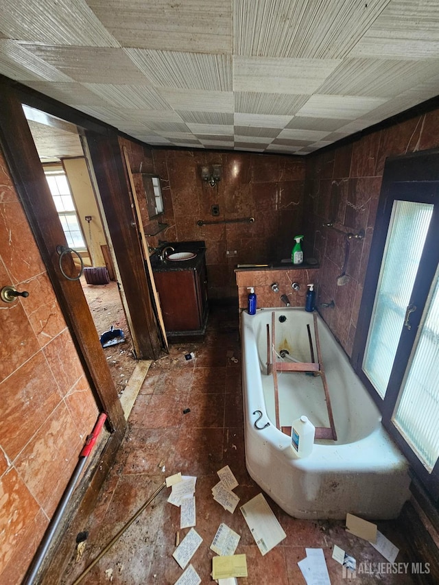 bathroom featuring tile walls, a bath, and vanity