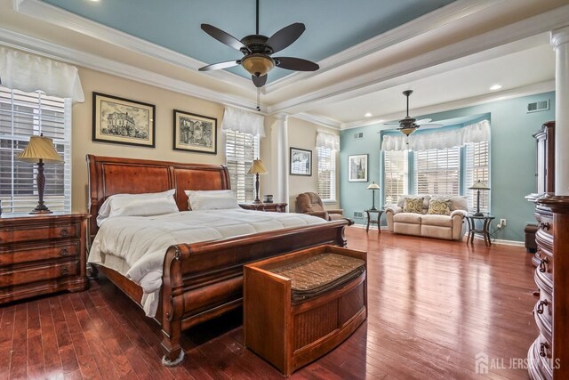 bedroom featuring wood-type flooring, a tray ceiling, crown molding, and ornate columns