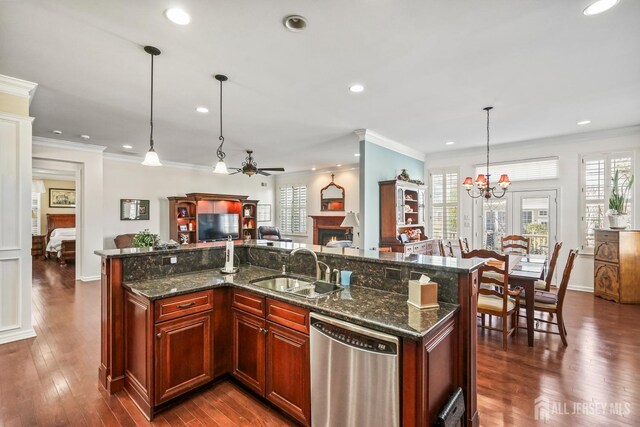 kitchen with a center island with sink, hanging light fixtures, dark stone counters, sink, and stainless steel dishwasher