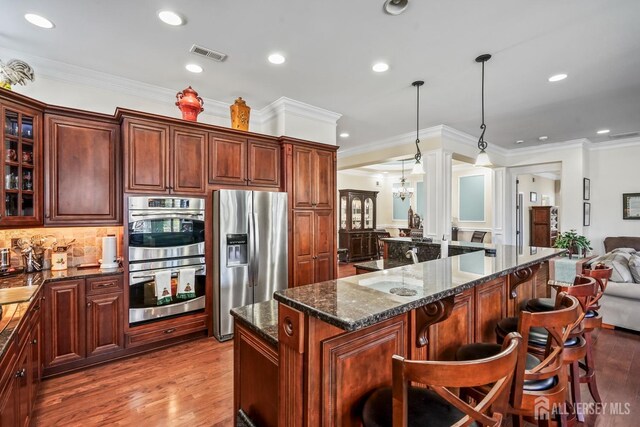 kitchen with a center island, light hardwood / wood-style floors, pendant lighting, crown molding, and appliances with stainless steel finishes