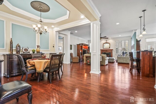 dining room with ornamental molding, dark hardwood / wood-style flooring, decorative columns, and ceiling fan with notable chandelier