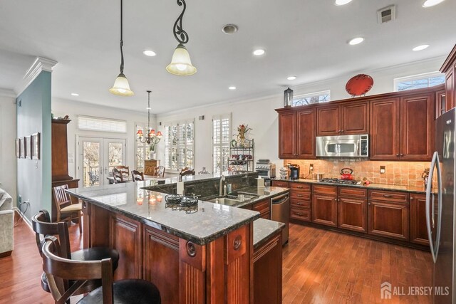 kitchen with pendant lighting, stainless steel appliances, a breakfast bar, a kitchen island with sink, and sink