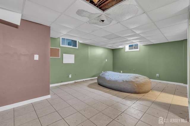 basement featuring baseboards, light tile patterned flooring, and a paneled ceiling