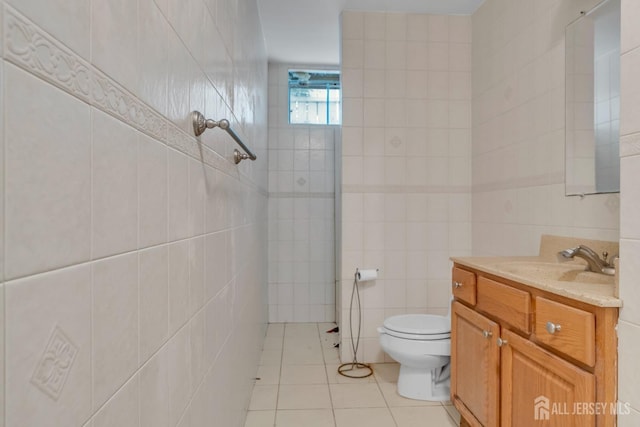 bathroom featuring a tile shower, tile patterned flooring, vanity, toilet, and tile walls