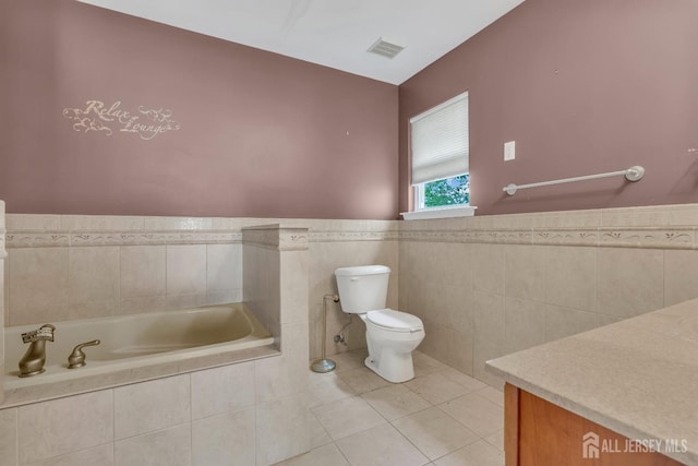 bathroom featuring toilet, tile patterned floors, a wainscoted wall, tile walls, and a garden tub
