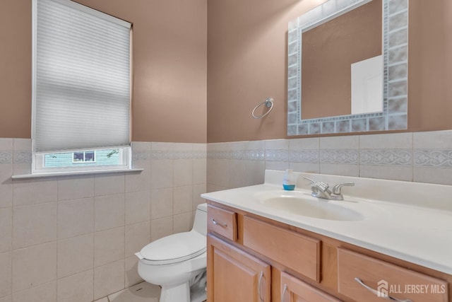 half bathroom with wainscoting, tile walls, vanity, and toilet