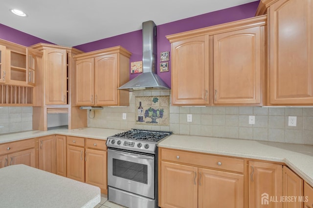 kitchen with wall chimney range hood, decorative backsplash, gas range, light brown cabinetry, and light countertops