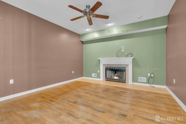 unfurnished living room featuring ceiling fan, baseboards, wood finished floors, a tile fireplace, and visible vents
