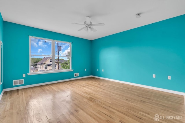 spare room with baseboards, ceiling fan, visible vents, and wood finished floors