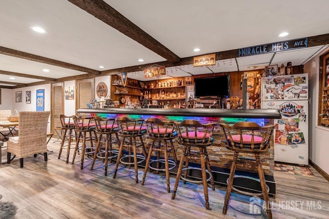 bar featuring beam ceiling, a bar, freestanding refrigerator, and wood finished floors