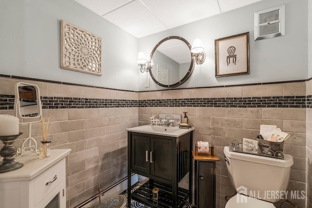 half bath with vanity, tile walls, toilet, and wainscoting