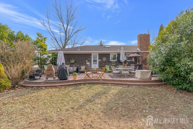 rear view of property featuring a wooden deck, outdoor dining area, and a chimney