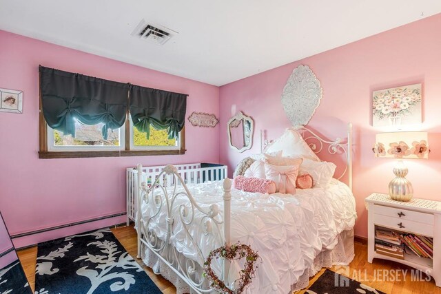 bedroom with visible vents, baseboard heating, and wood finished floors