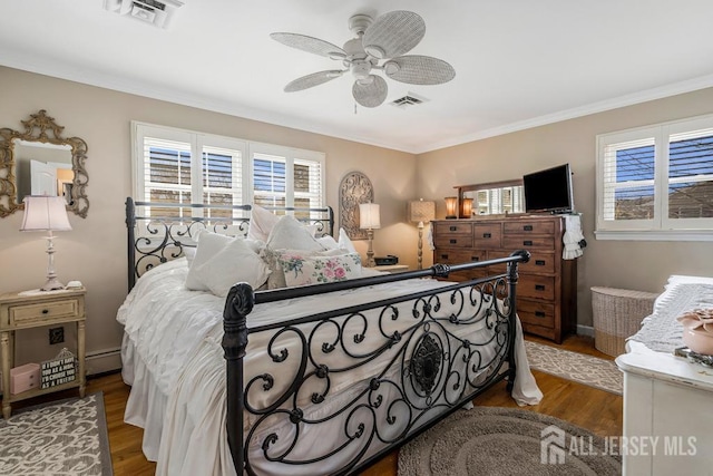 bedroom featuring visible vents, crown molding, baseboards, and wood finished floors