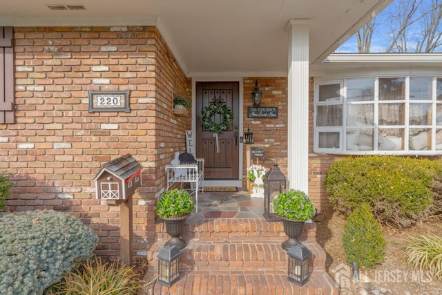 doorway to property with visible vents, brick siding, and covered porch