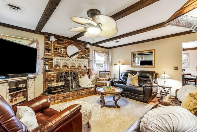 living room with a ceiling fan, beamed ceiling, a fireplace, and visible vents