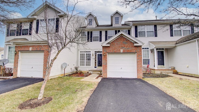 townhome / multi-family property with driveway, a front yard, a garage, and brick siding