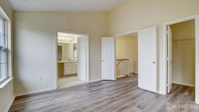 unfurnished bedroom featuring connected bathroom, a spacious closet, vaulted ceiling, light hardwood / wood-style flooring, and a closet