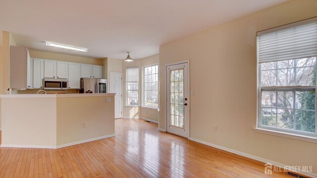 kitchen with white cabinetry, light wood-type flooring, a healthy amount of sunlight, and appliances with stainless steel finishes