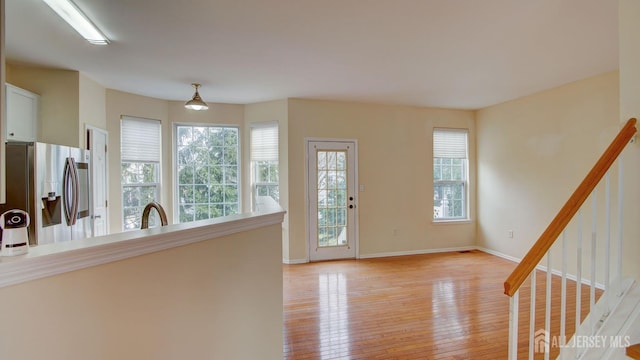 interior space featuring sink, stainless steel fridge with ice dispenser, hanging light fixtures, and light wood-type flooring