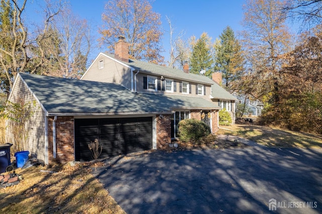 view of front of property featuring an attached garage, brick siding, driveway, roof with shingles, and a chimney