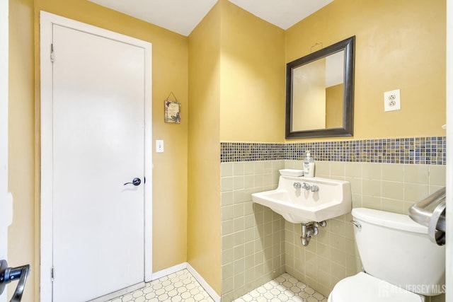 half bathroom with toilet, a wainscoted wall, a sink, and tile walls