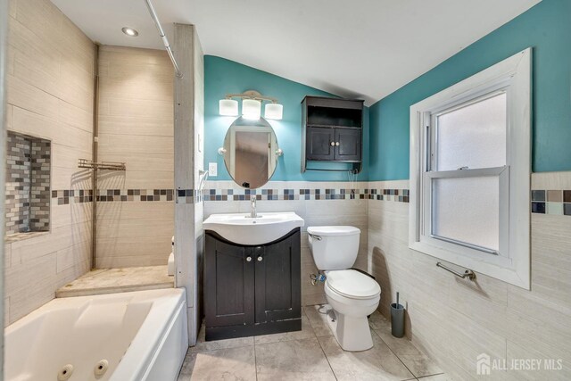 bathroom featuring lofted ceiling, tile walls, a tub to relax in, vanity, and toilet