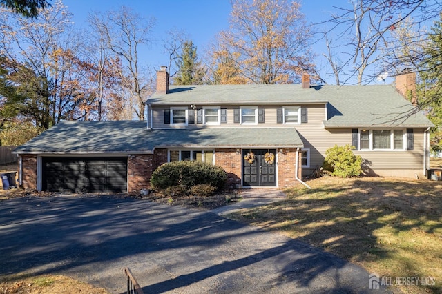 view of front of house featuring driveway, brick siding, a chimney, and an attached garage