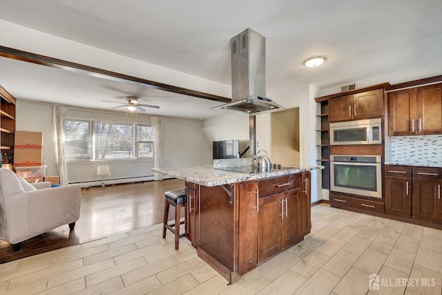 kitchen with a breakfast bar, appliances with stainless steel finishes, light stone counters, an island with sink, and island exhaust hood