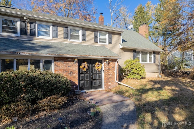 view of front of house with brick siding, a chimney, a shingled roof, and a front yard