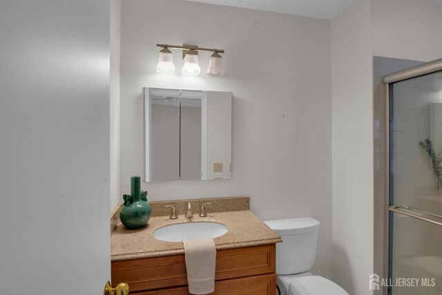 bathroom with a shower with door, vanity, and toilet