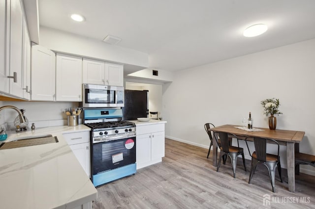 kitchen with light stone counters, light wood-style flooring, a sink, white cabinets, and appliances with stainless steel finishes