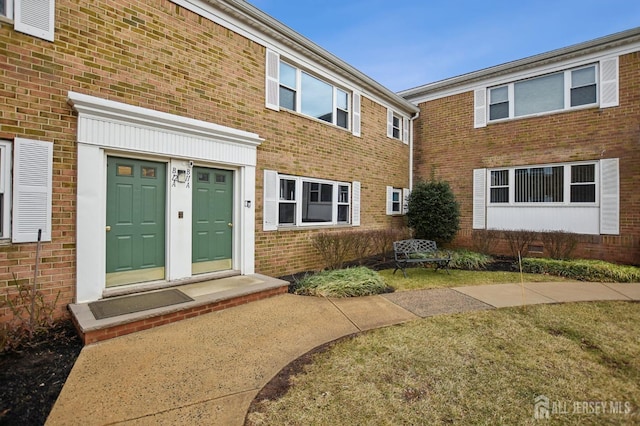 view of exterior entry featuring brick siding and a lawn