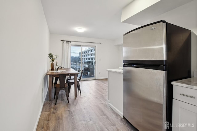 kitchen with baseboards, white cabinets, wood finished floors, freestanding refrigerator, and light countertops