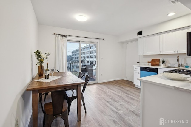 kitchen featuring light countertops, light wood-style floors, white cabinets, a sink, and dishwashing machine