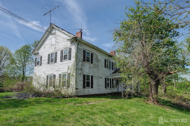 back of house with a chimney and a yard