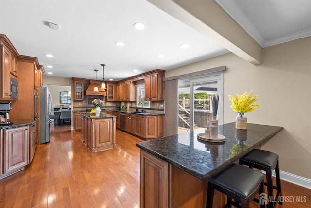 kitchen featuring premium range hood, brown cabinetry, a kitchen island, glass insert cabinets, and appliances with stainless steel finishes