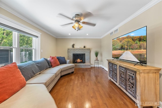 living area with ceiling fan, hardwood / wood-style floors, a brick fireplace, ornamental molding, and recessed lighting