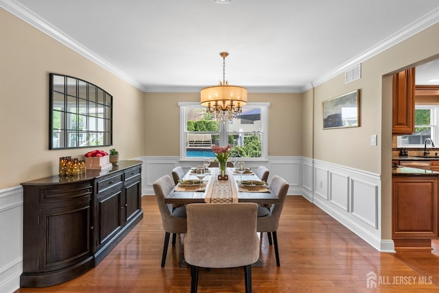 dining area featuring a chandelier, a wainscoted wall, a decorative wall, wood finished floors, and ornamental molding