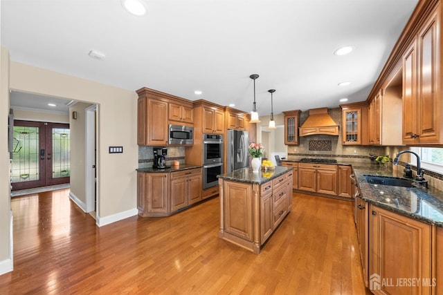 kitchen with stainless steel appliances, premium range hood, a sink, brown cabinetry, and recessed lighting
