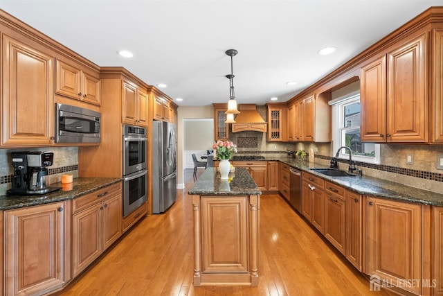 kitchen with a sink, stainless steel appliances, custom exhaust hood, light wood-style flooring, and a center island
