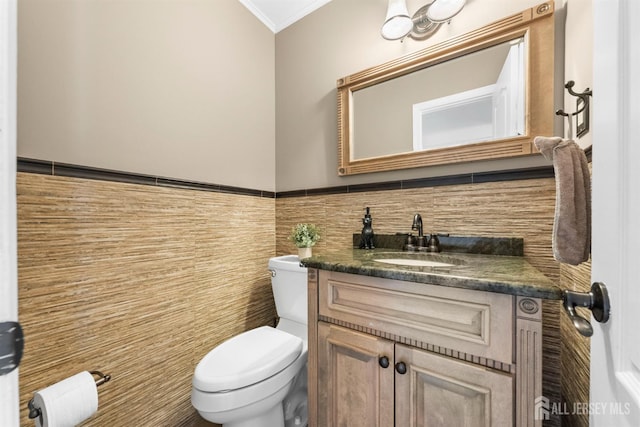 bathroom featuring toilet, ornamental molding, vanity, tile walls, and wainscoting