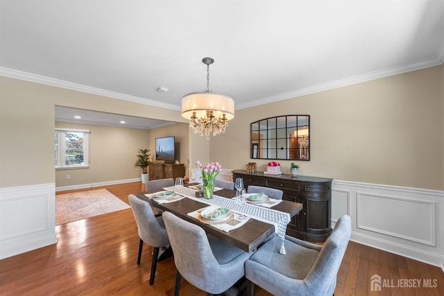 dining room featuring a chandelier, wood finished floors, ornamental molding, and wainscoting