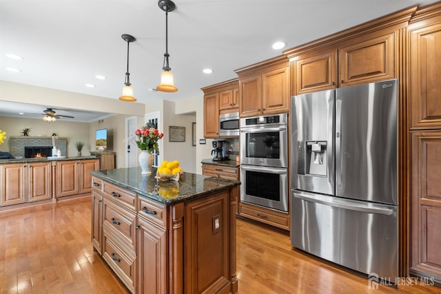 kitchen with stainless steel appliances, brown cabinets, light wood-style flooring, a center island, and recessed lighting