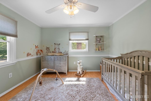 bedroom with multiple windows, wood finished floors, a nursery area, ornamental molding, and ceiling fan