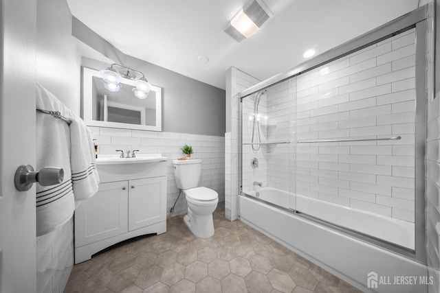bathroom featuring tile walls, combined bath / shower with glass door, vanity, toilet, and tile patterned flooring